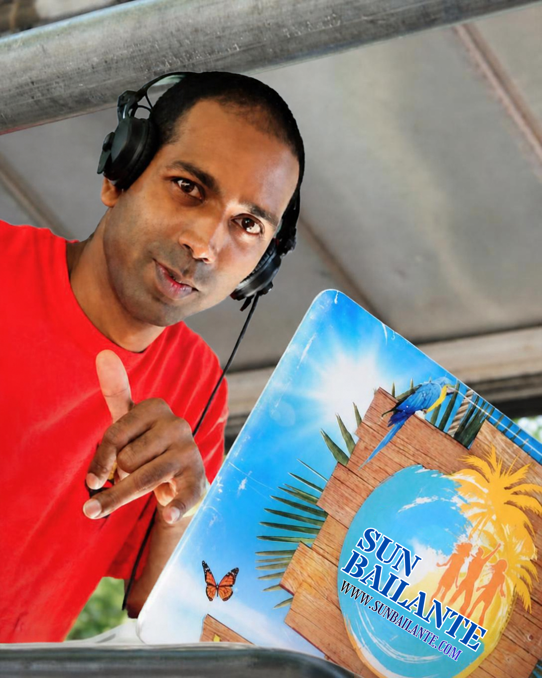 DJ Jay Sun Bailante au casque, t-shirt rouge, levant le pouce devant son stand Sun Bailante